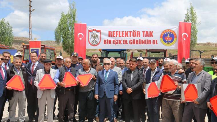 Reflektör ve uyarı levhaları tutan kalabalık bir grup, arka planda afiş ve bayraklar var.
