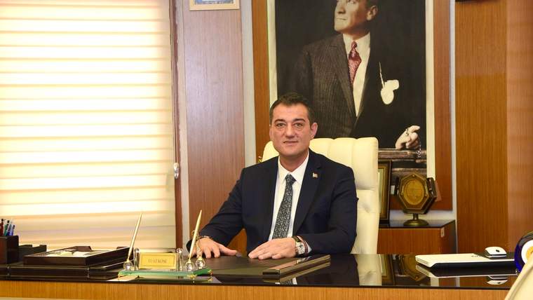 Bir masanın arkasında oturan bir kişi, duvarda Atatürk'ün portresi asılı.