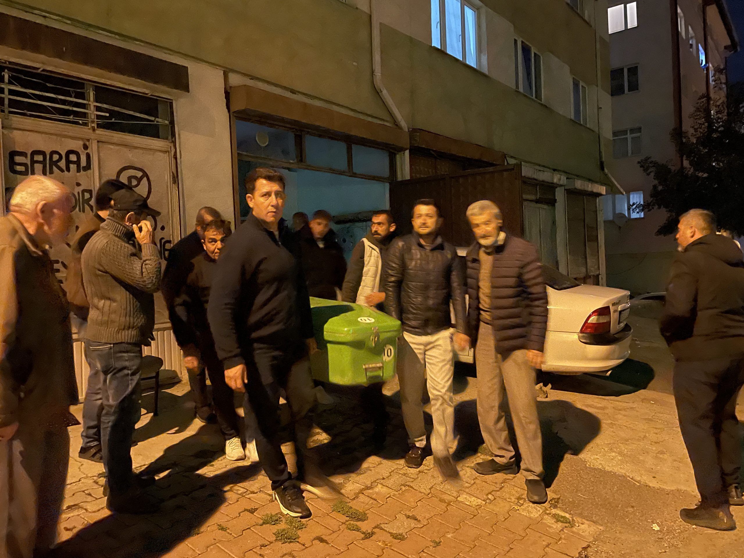 Bir grup erkek, yeşil bir tabutu kaldırarak bir binanın önünden geçiyor.