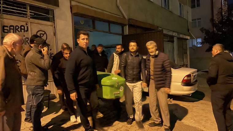 Bir grup erkek, yeşil bir tabutu kaldırarak bir binanın önünden geçiyor.