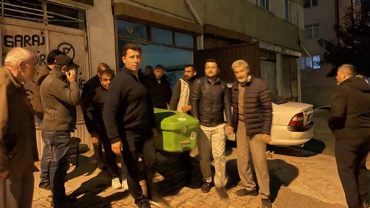 Bir grup erkek, yeşil bir tabutu kaldırarak bir binanın önünden geçiyor.