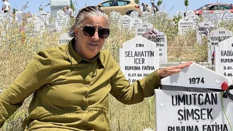 Bir kadın, mezar taşlarının önünde oturmuş, bir mezar taşına bakıyor.