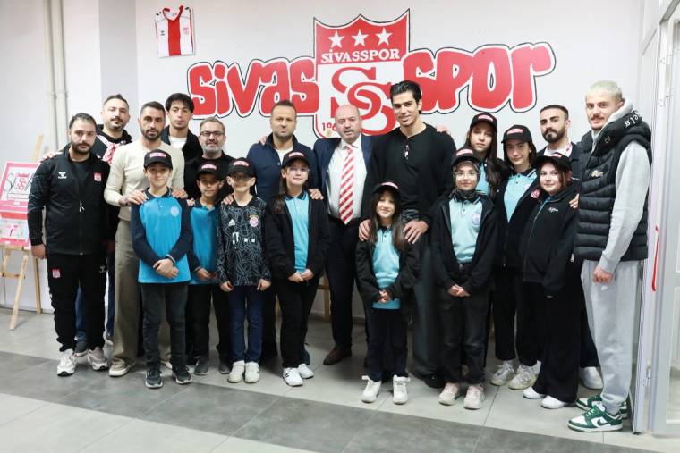Sivasspor'un logosunun arkasında, minik taraftarlar ve kulüp yetkilileri bir arada poz veriyor.