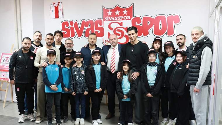 Sivasspor'un logosunun arkasında, minik taraftarlar ve kulüp yetkilileri bir arada poz veriyor.