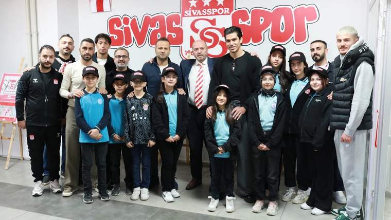 Sivasspor'un logosunun arkasında, minik taraftarlar ve kulüp yetkilileri bir arada poz veriyor.