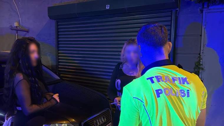 Gece bir otomobilin yanında, sırtında “Trafik Polisi” yazan reflektif yelekli görevli iki kadınla konuşuyor.