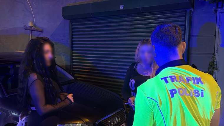 Gece bir otomobilin yanında, sırtında “Trafik Polisi” yazan reflektif yelekli görevli iki kadınla konuşuyor.