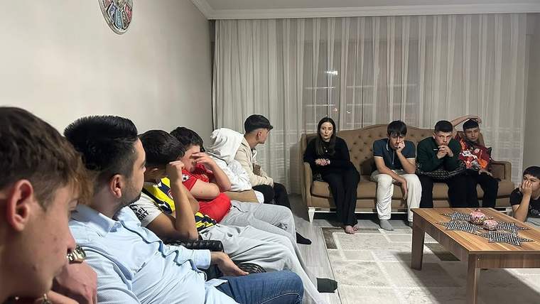 Bir grup genç, bir oturma odasında bir araya gelmiş, bir kişi onlara konuşuyor.