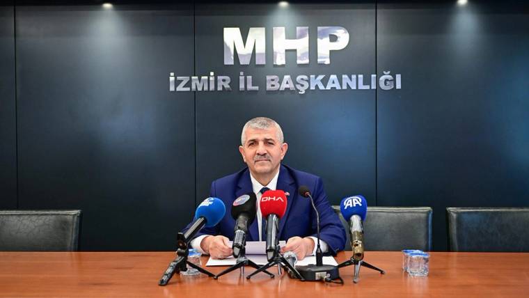 Üzerinde “MHP İzmir İl Başkanlığı” yazan salonda, bir kişi masa başında çok sayıda mikrofonla konuşuyor.