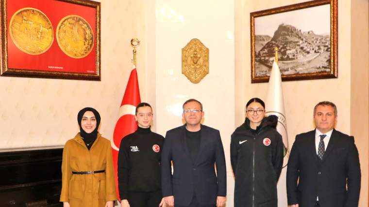 İç mekânda Türk bayrağı ve beyaz bayrak önünde duran beş kişi, arkada piyano ve tablolarla görülüyor.