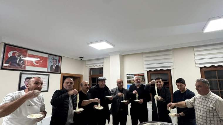 Bir grup erkek, masanın etrafında tel helva yerken gülümseyerek poz veriyor.