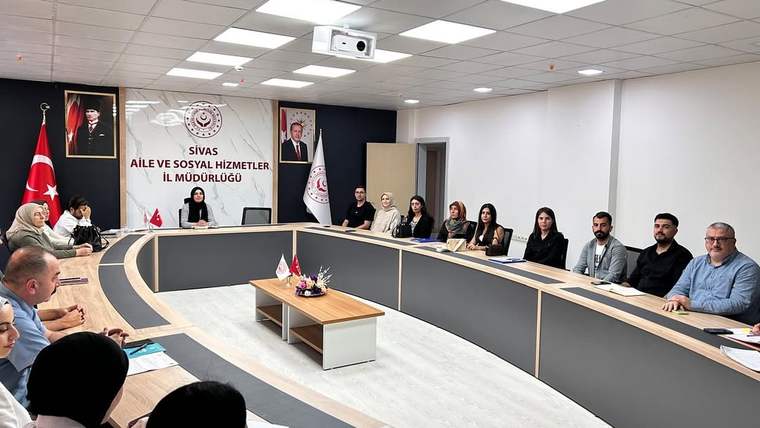 Toplantı salonunda çok sayıda kişi U biçimli masanın çevresinde oturuyor; masada Türk bayrağı bulunuyor.
