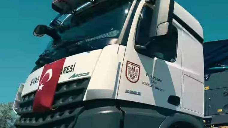 Üzerinde Türk bayrağı ve Sivas Belediyesi logosu bulunan bir kamyon, açık havada duruyor.