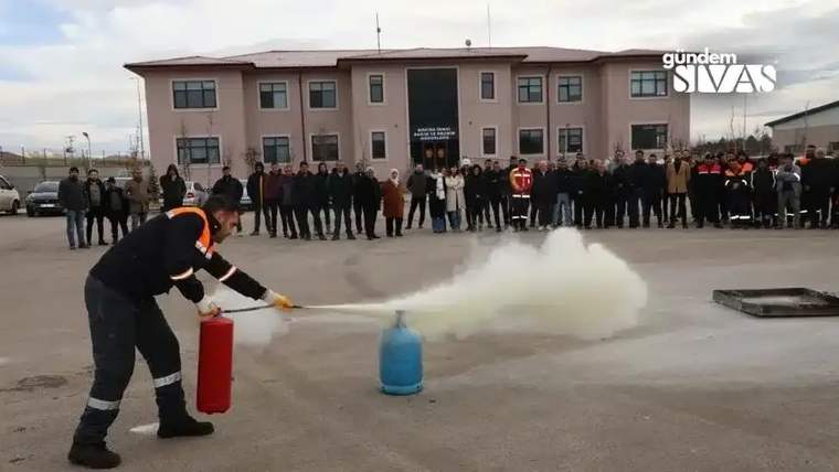 Bir kişi, yangın tatbikatında yangın söndürücü ile mavi bir silindirin üzerine köpük püskürtüyor.