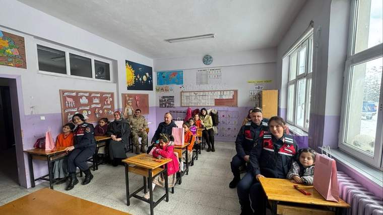 Sınıfta sıralarında oturan çocuklar ve yetişkinler, ön sırada bir çocukla birlikte kameraya bakıyor.