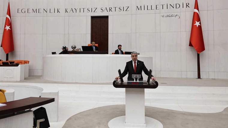 Bir kişi, TBMM Genel Kurulu'nda kürsüde konuşuyor, arka planda Türk bayrağı ve milletvekilleri var.