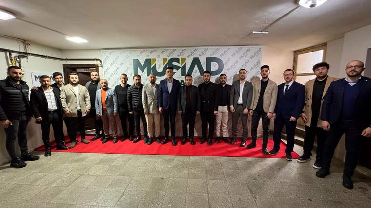 MÜSİAD yazılı pankartın önünde, kapalı salonda yan yana duran bir grup erkek