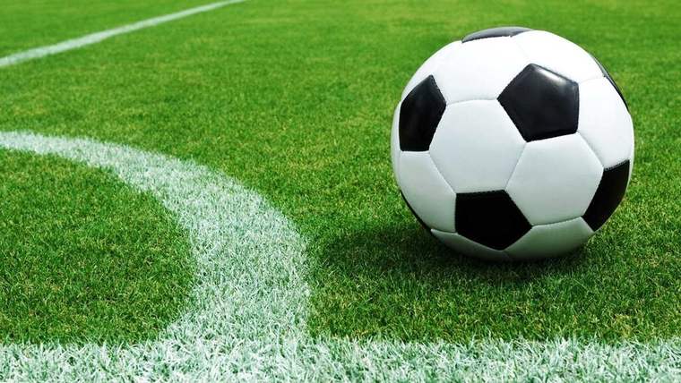 Yeşil futbol sahasında, beyaz ve siyah renkte bir futbol topu, kenar çizgisine yakın bir konumda duruyor.