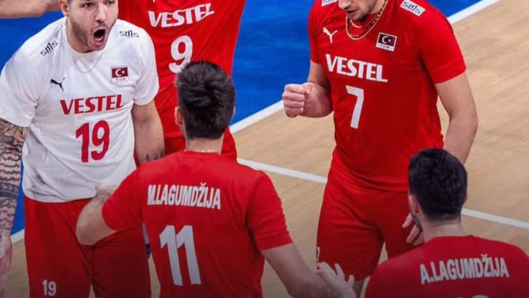 Kırmızı ve beyaz formalar giymiş voleybol takımı oyuncuları, sevinç içinde bir araya gelmiş.