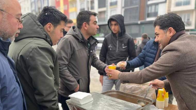 Bir grup insan, çorba ikramı yapan bir kişiden çorba alıyor.