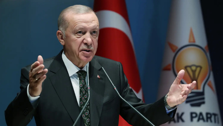 Kürsüde konuşan bir kişi, arkasında Türk bayrağı ve AK Parti logosu var.
