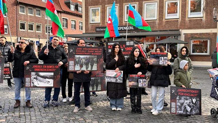 Azerbaycan bayrakları taşıyan bir grup, üzerinde “Justice for Khojaly” yazılı dövizlerle bina önünde duruyor.