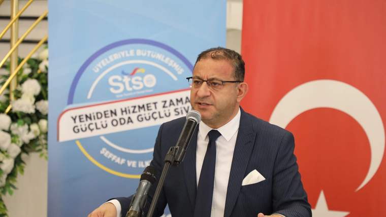 Kürsüde mikrofonla konuşan takım elbiseli bir erkek; arkasında STSO yazılı pankart ve Türk bayrağı bulunuyor.