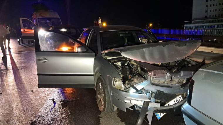 Üst geçitte çarpışmış bir aracın ön kısmı hasar görmüş, kapısı açık durumda.