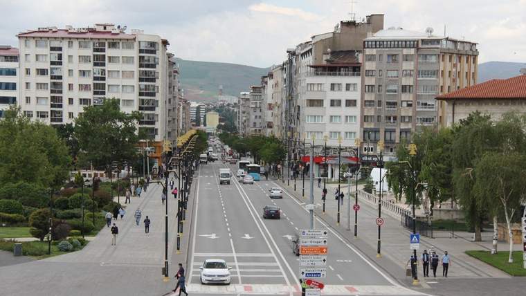 Sivas'ta geniş bir cadde, her iki yanında apartmanlar ve ağaçlar yer alıyor.