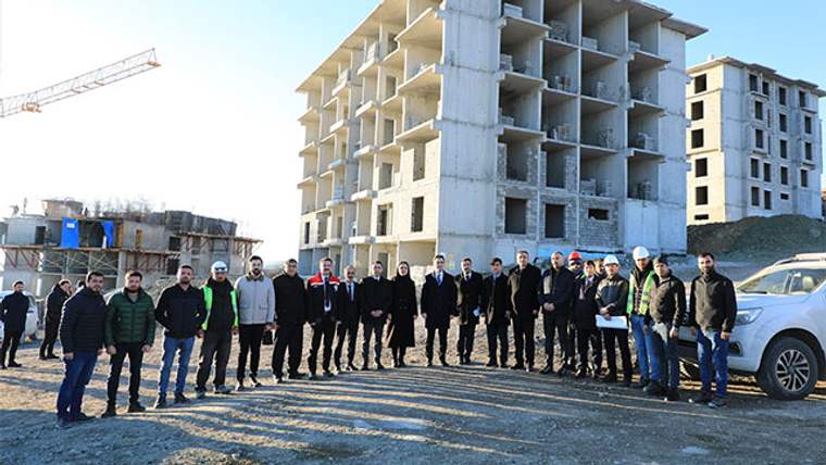 İnşaatı süren çok katlı betonarme binaların önünde, kalabalık bir grup insan yan yana duruyor.
