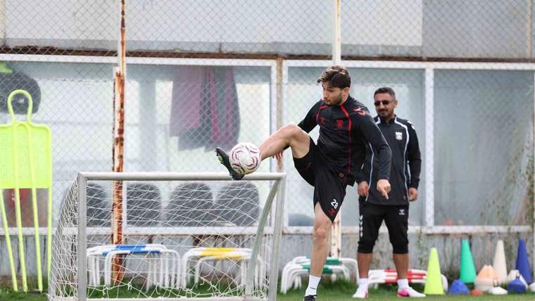Siyah-kırmızı spor kıyafetli futbolcu, antrenman sahasında topa vururken arkasında bir kişi bekliyor.