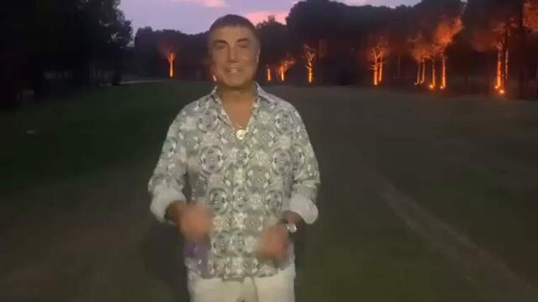 Alacakaranlıkta ağaçlarla çevrili alanda desenli gömlek ve açık renk pantolon giyen bir kişi duruyor.