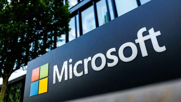 Modern bir binanın önündeki panoda renkli Microsoft logosu ve beyaz Microsoft yazısı görülüyor.