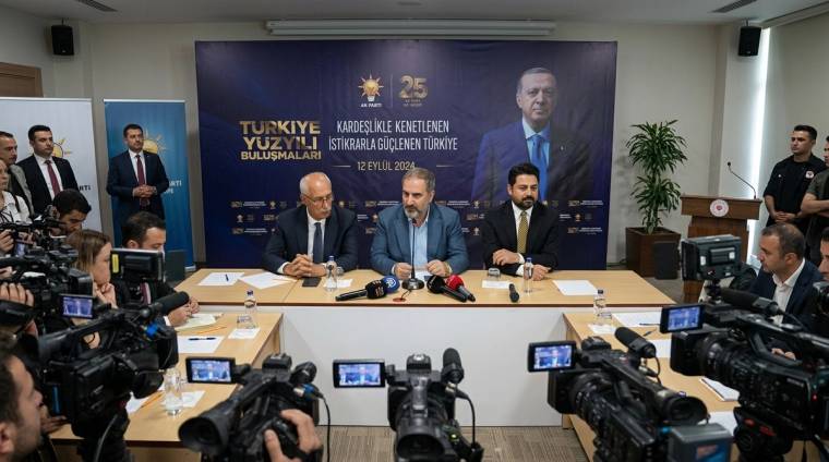 Bir salonda üç kişi masa başında otururken, önlerinde mikrofonlar ve çok sayıda kamera bulunuyor.