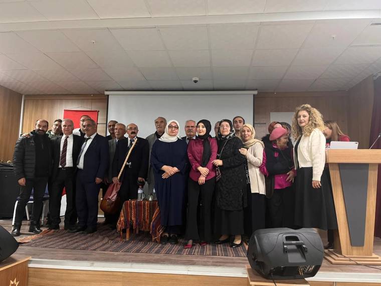 Bir grup insan, sahnede bir araya gelerek poz veriyor; arka planda bir projeksiyon perdesi var.