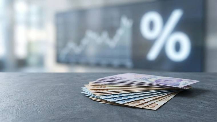 Masa üzerinde üst üste duran banknotlar, arka planda bulanık grafik ve büyük yüzde işaretiyle birlikte görülüyor.