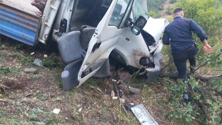 Şarampole yan yatmış traktör yüklü kamyonetin ön kısmı ve yanında duran bir kişi görülüyor.