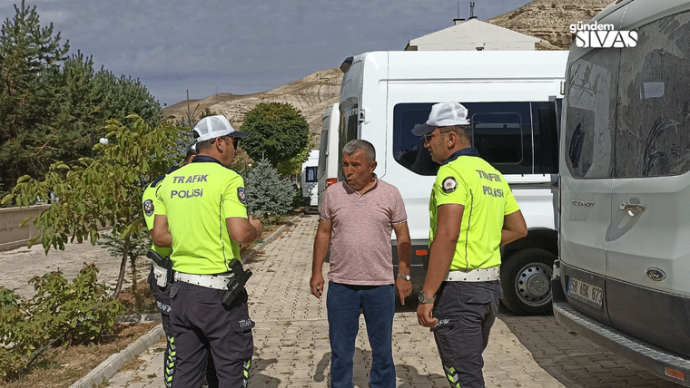 İki trafik polisi, beyaz minibüslerin yanında duran bir erkekle kaldırımda konuşuyor.
