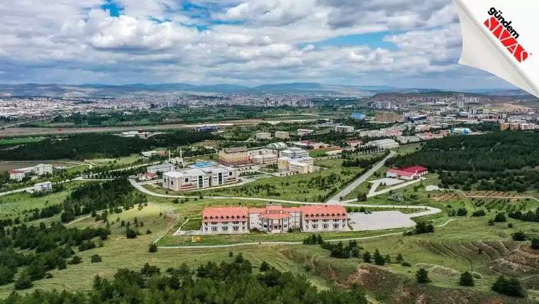 Yeşil alanlar ve binalarla çevrili bir kampüs manzarası, uzaktan çekilmiş.