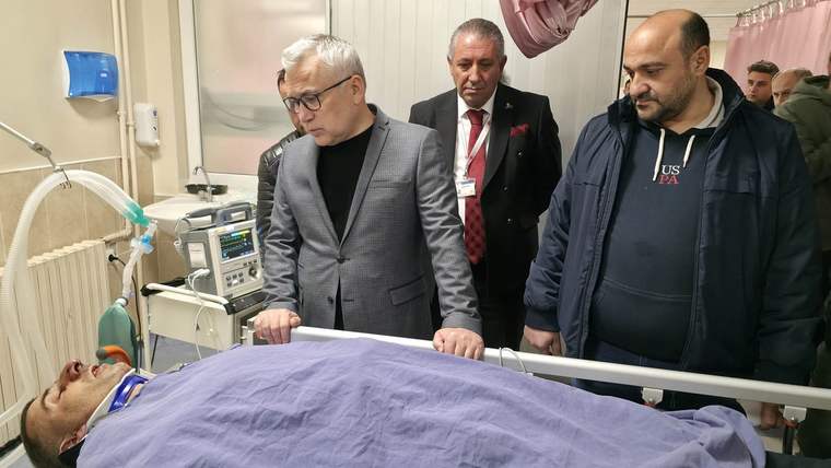 Hastanede yatan yaralı bir kişi, yanında üç kişi duruyor ve durumu inceliyor.
