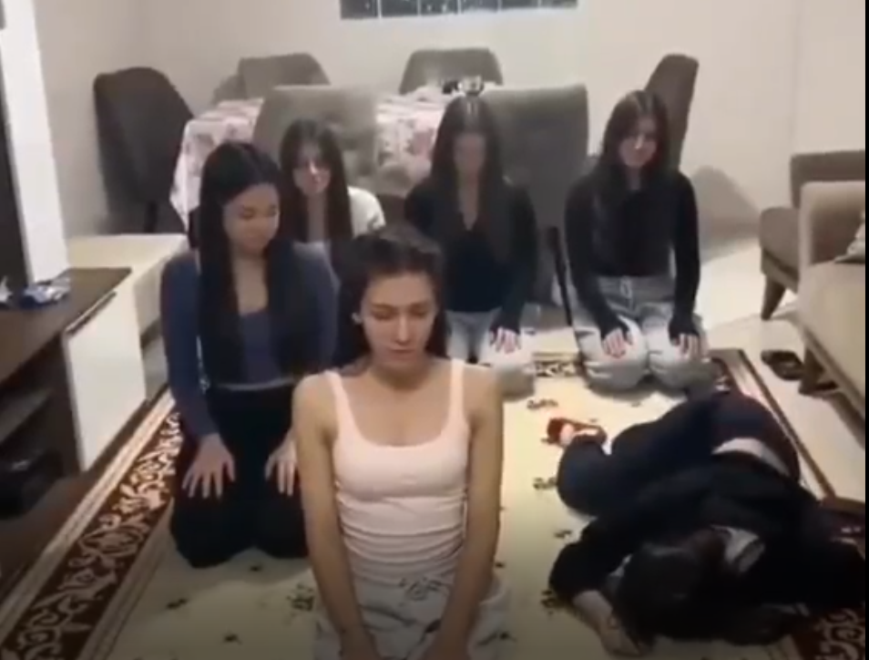Bir grup kadın, bir halının üzerinde oturmuş ve farklı pozisyonlarda duruyorlar.