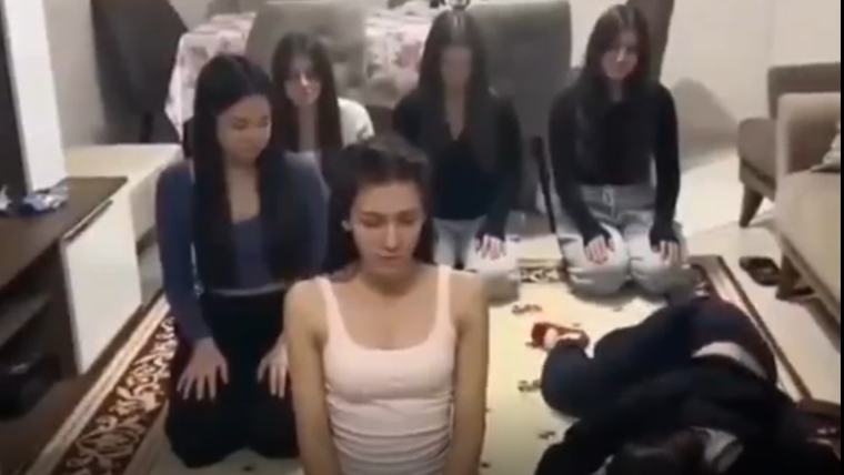 Bir grup kadın, bir halının üzerinde oturmuş ve farklı pozisyonlarda duruyorlar.