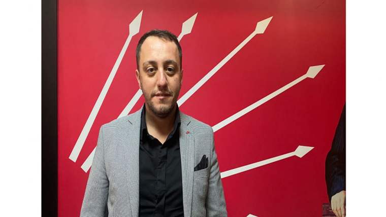 Kırmızı zemin üzerindeki beyaz ok biçimli çizgilerin önünde duran, gri ceketli bir kişi görülüyor.