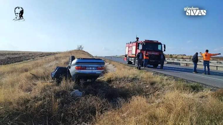 Yol kenarındaki otluk alanda duran otomobilin yanında itfaiye aracı ve birkaç kişi görülüyor.