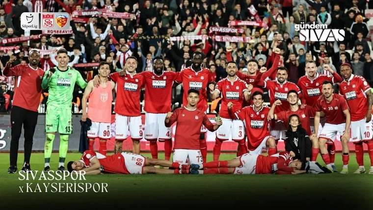 Kırmızı formalı futbolcular, yeşil formalı kaleci ve taraftarlar saha kenarında birlikte poz veriyor.