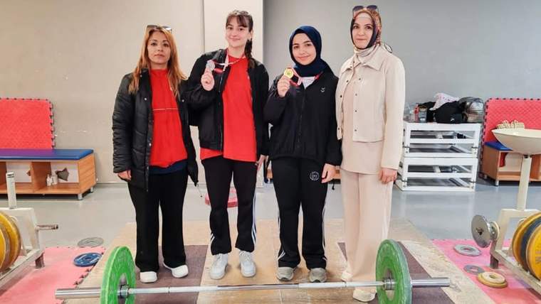 Halter salonunda dört kadın, madalya ve kupayla birlikte, yerdeki ağırlık barının arkasında duruyor.