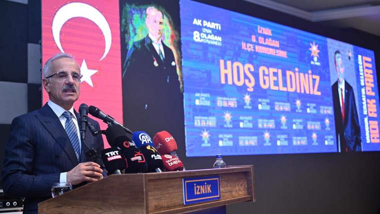 Bir kişi, mikrofonun önünde konuşuyor; arka planda Türk bayrağı ve hoş geldiniz yazısı var.