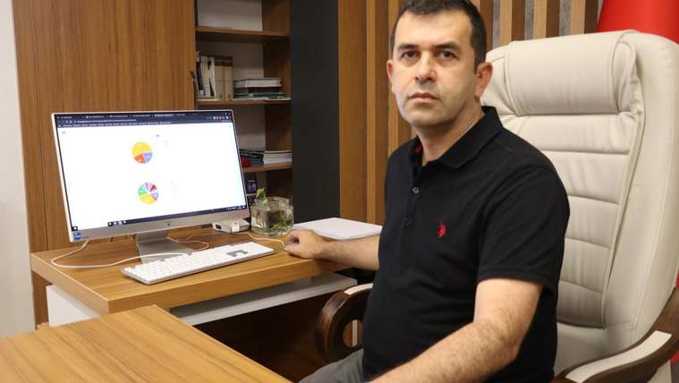 Masa başında oturan bir kişi, bilgisayar ekranındaki renkli grafiklerin yanında kameraya bakıyor.