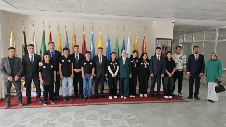 Öğrenciler, madalyalarıyla birlikte bir grup halinde, arka planda bayraklarla poz veriyor.