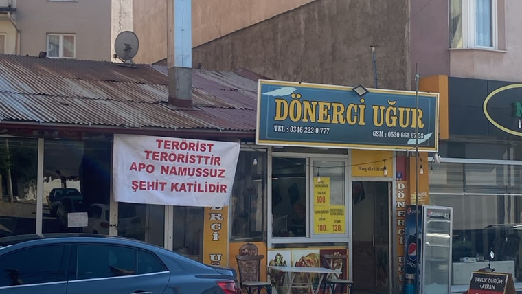 Dönerci Uğur dükkânının önünde, üzerinde protesto ifadeleri bulunan bir pankart asılı duruyor.